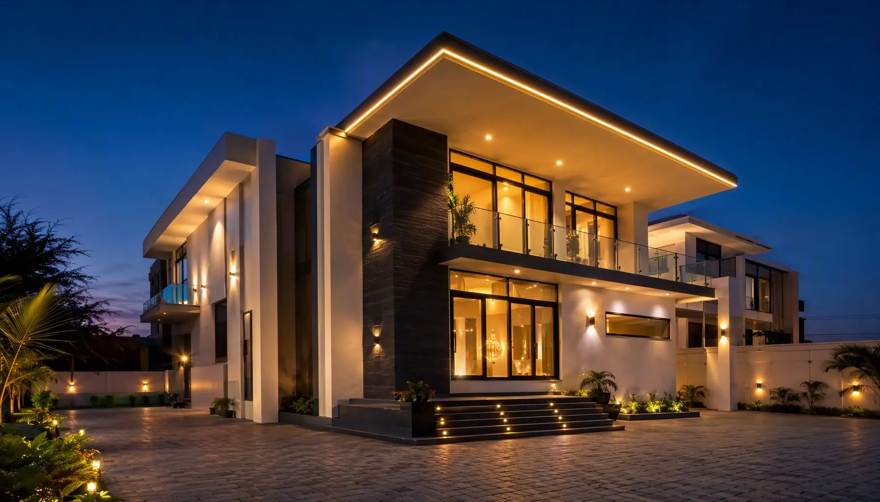 A modern two-storey home at dusk, its deep roof edged in warm light, with a stacked-stone feature column, tall glazing and a glass-railed balcony.