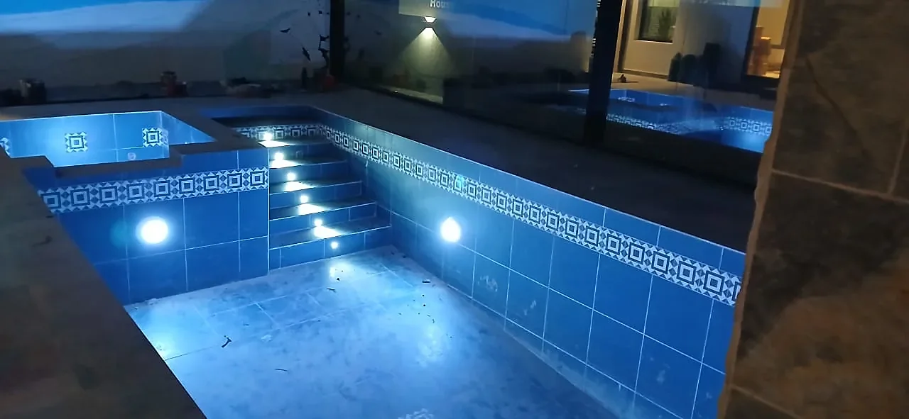 The finished pool at night, with underwater lights and lit steps reflecting off the blue tiling.