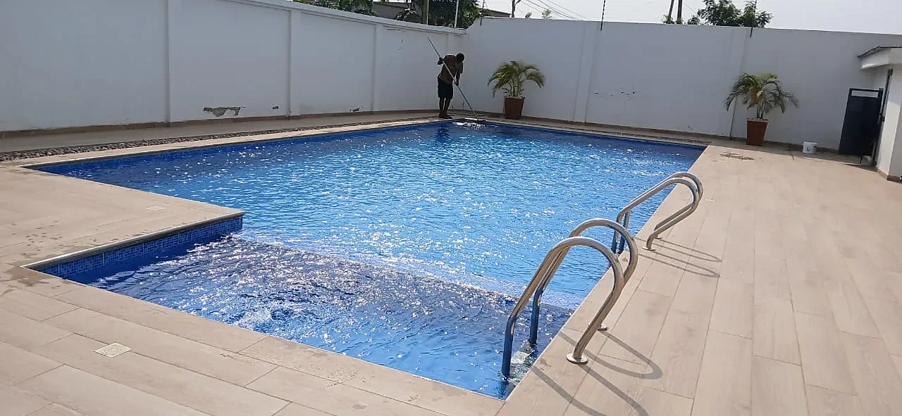 A finished swimming pool with clear blue water, stainless handrails and a timber-effect tiled surround.