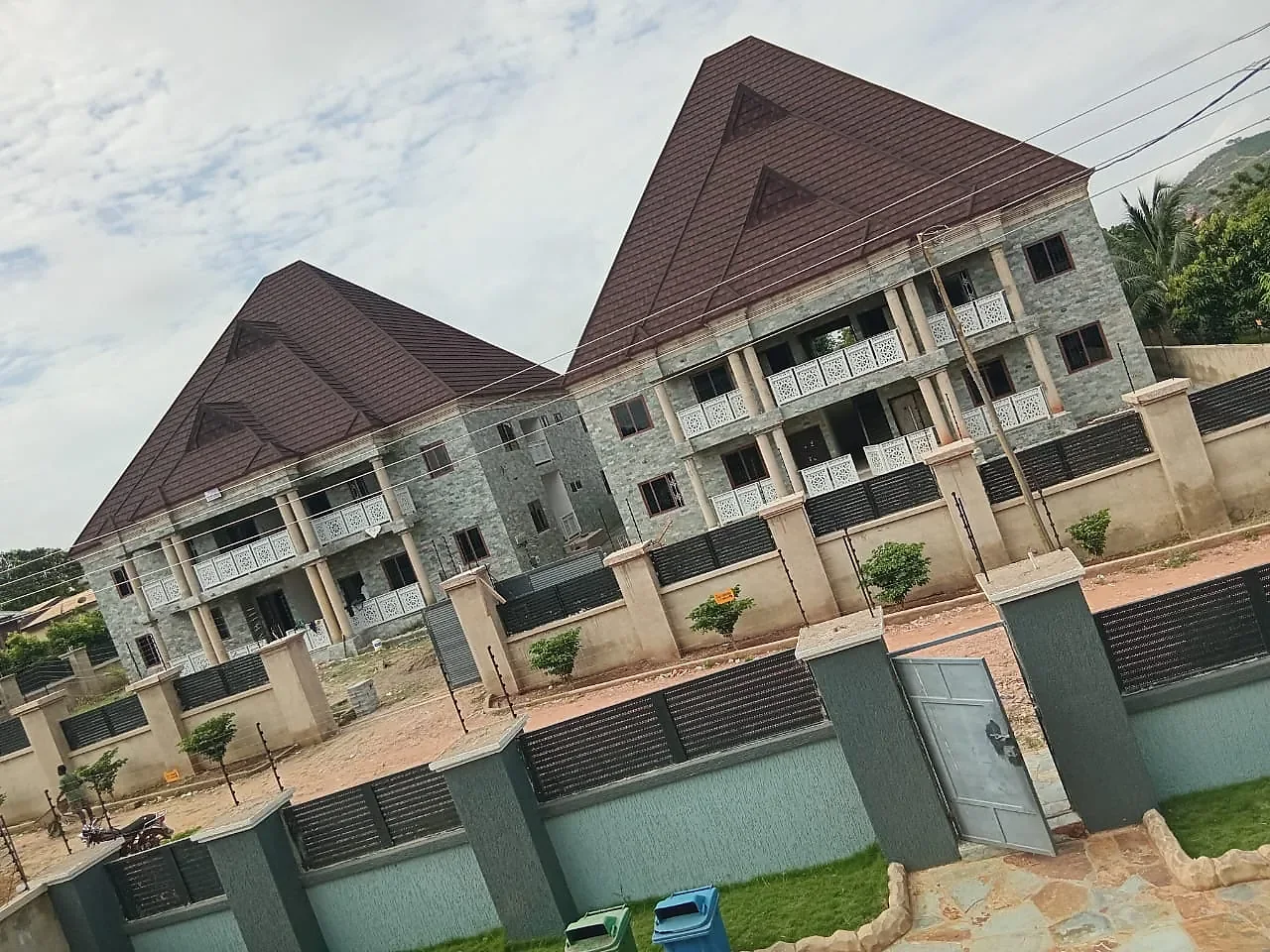 Two two-storey blocks faced in cut natural stone, with brown roofs, gates and planted grounds.