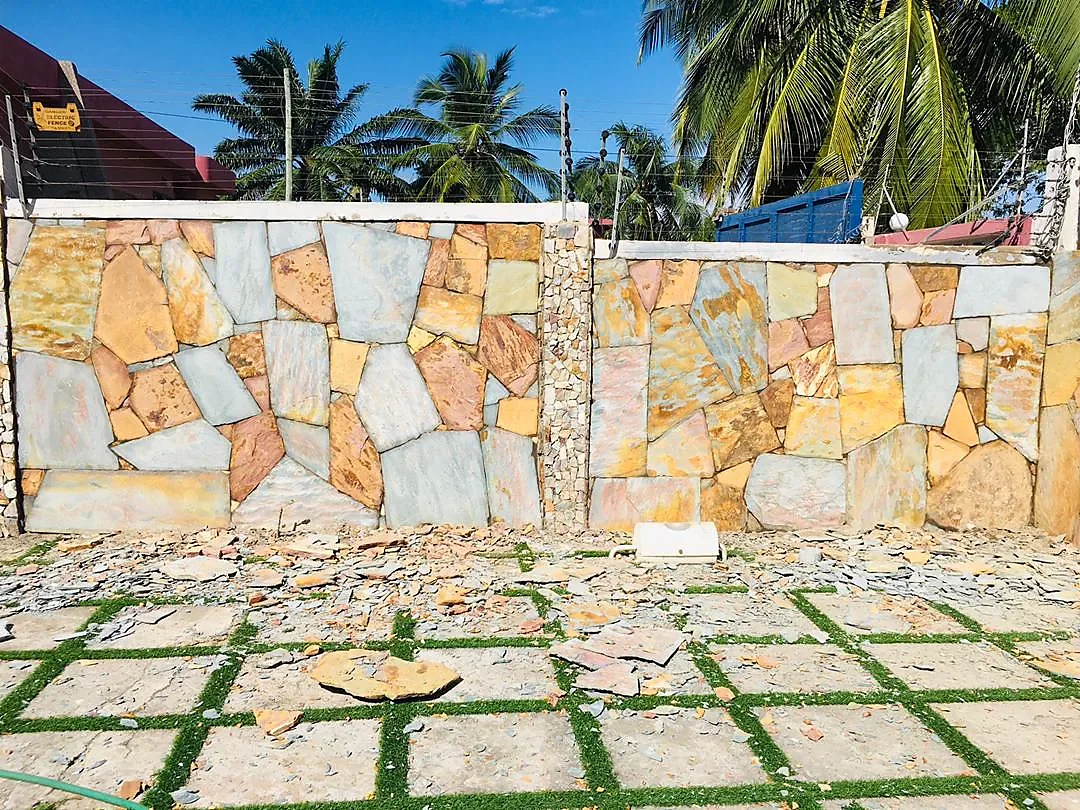 A boundary wall clad in mixed cut stone, with grass-jointed paving slabs laid in front of it.